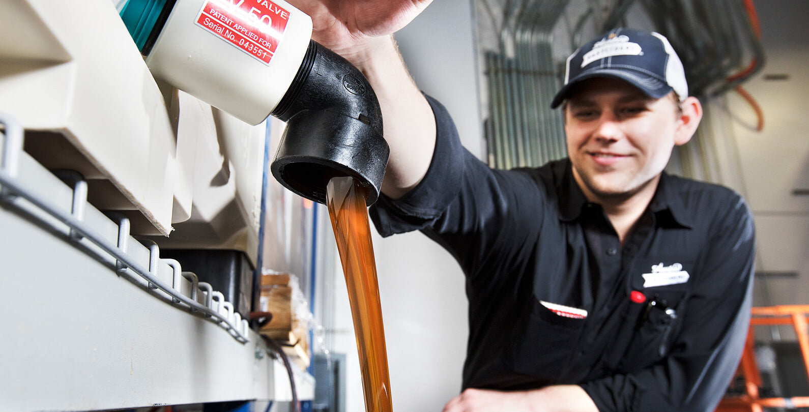 A smiling man in an Eastciders uniform drains apple juice from a tank on a shelf