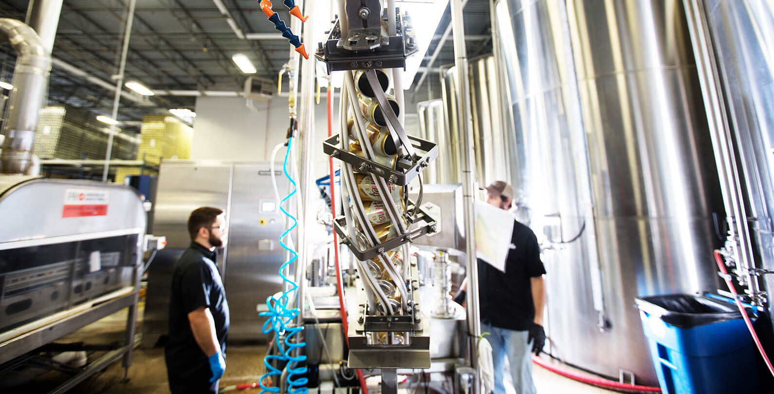 Two young men surrounded by machinery, working on large scale brewing equipment